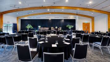 Sala de conferências com mesas redondas, cadeiras pretas e palco com cortinas.