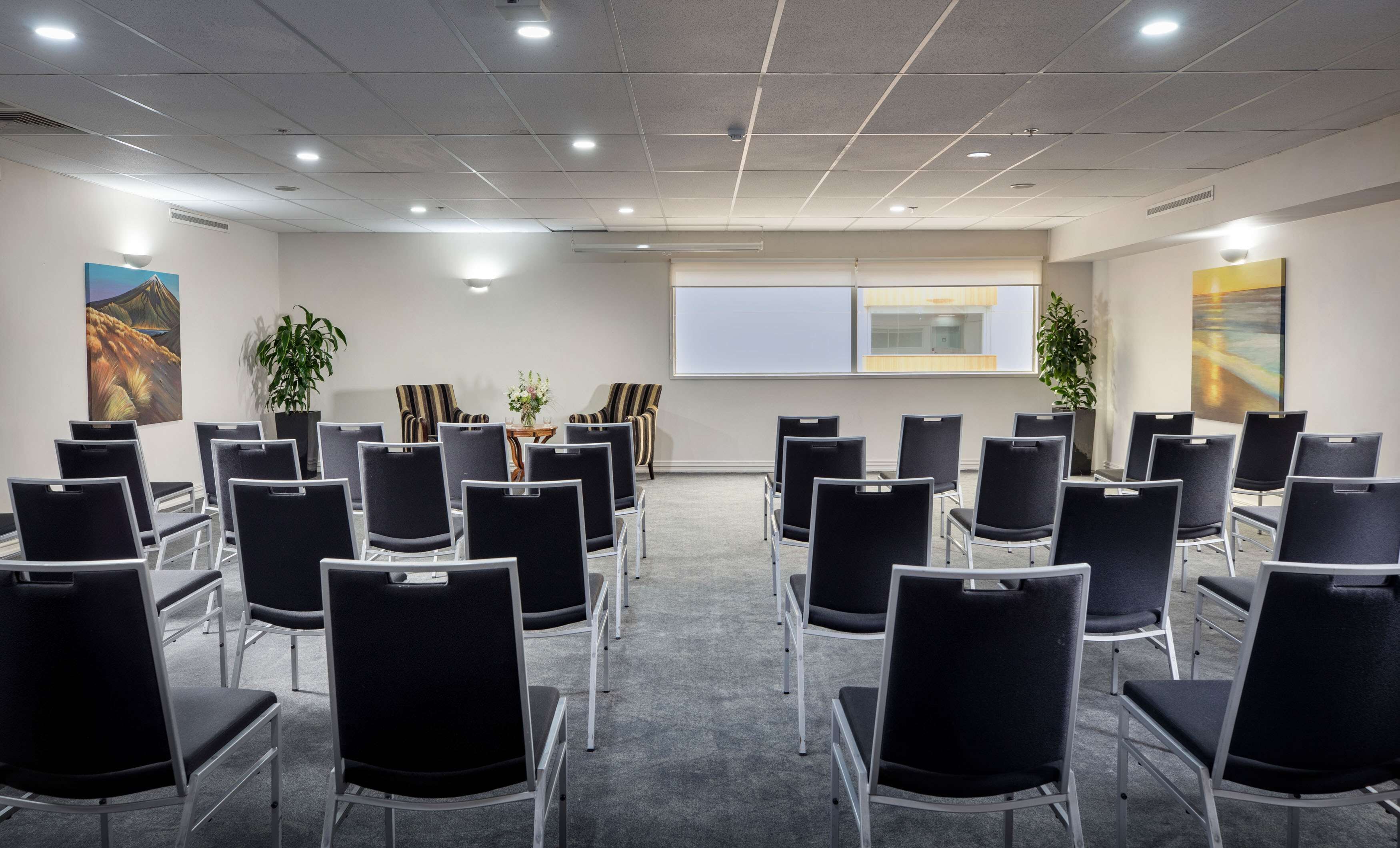 A conference room with rows of chairs, a projector screen, and two potted plants.