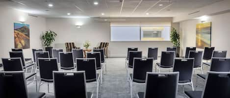 A conference room with rows of chairs, a projector screen, and two potted plants.
