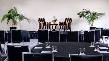 Uma sala de conferências com uma mesa redonda, cadeiras pretas e duas plantas em vasos.