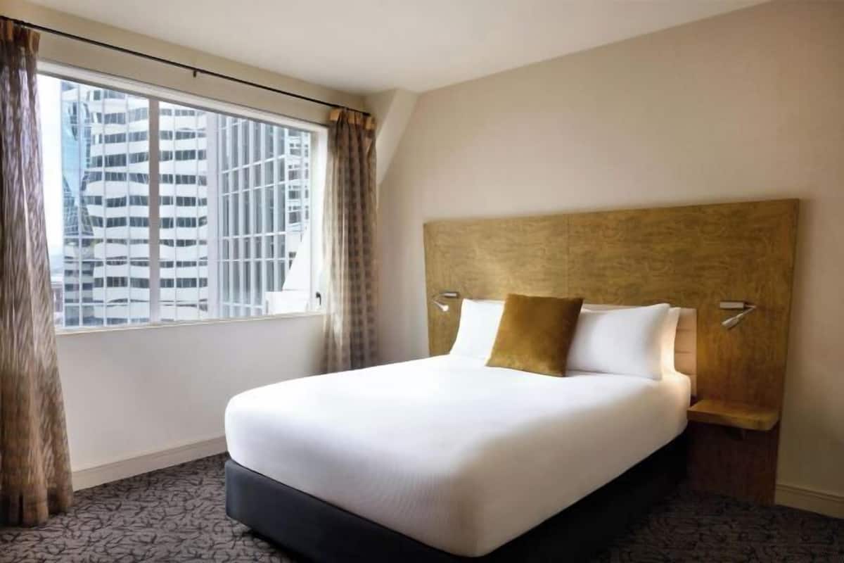 A hotel room with a large bed, a headboard, and a window with curtains.
