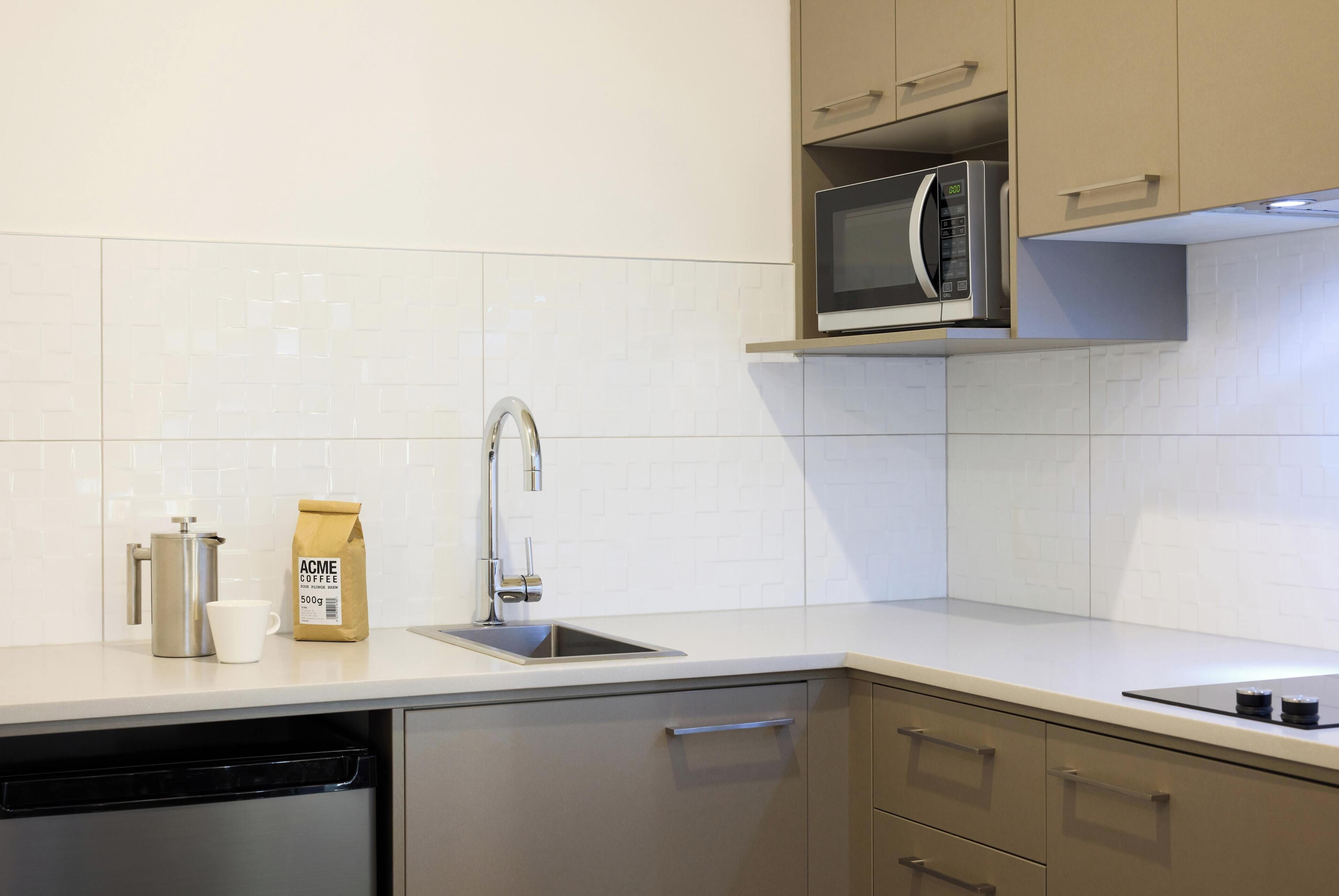 A modern kitchen with a dishwasher, a coffee maker, a bag of coffee, a microwave, and a sink.