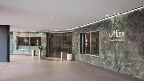 A modern hotel lobby with a marble wall, glass doors, and potted plants. - Adina CityLife Wellington (Wellington)