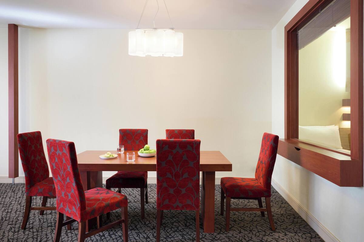 Un'area pranzo con un tavolo in legno, sei sedie rosse imbottite, un lampadario e una finestra con vista.