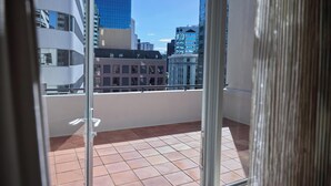 A balcony with a tiled floor, a glass door, and a view of city buildings. - Adina CityLife Wellington (Wellington)