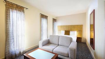 Habitación de hotel con sofá, una mesita, cabecera con lámparas y un espejo en la pared.