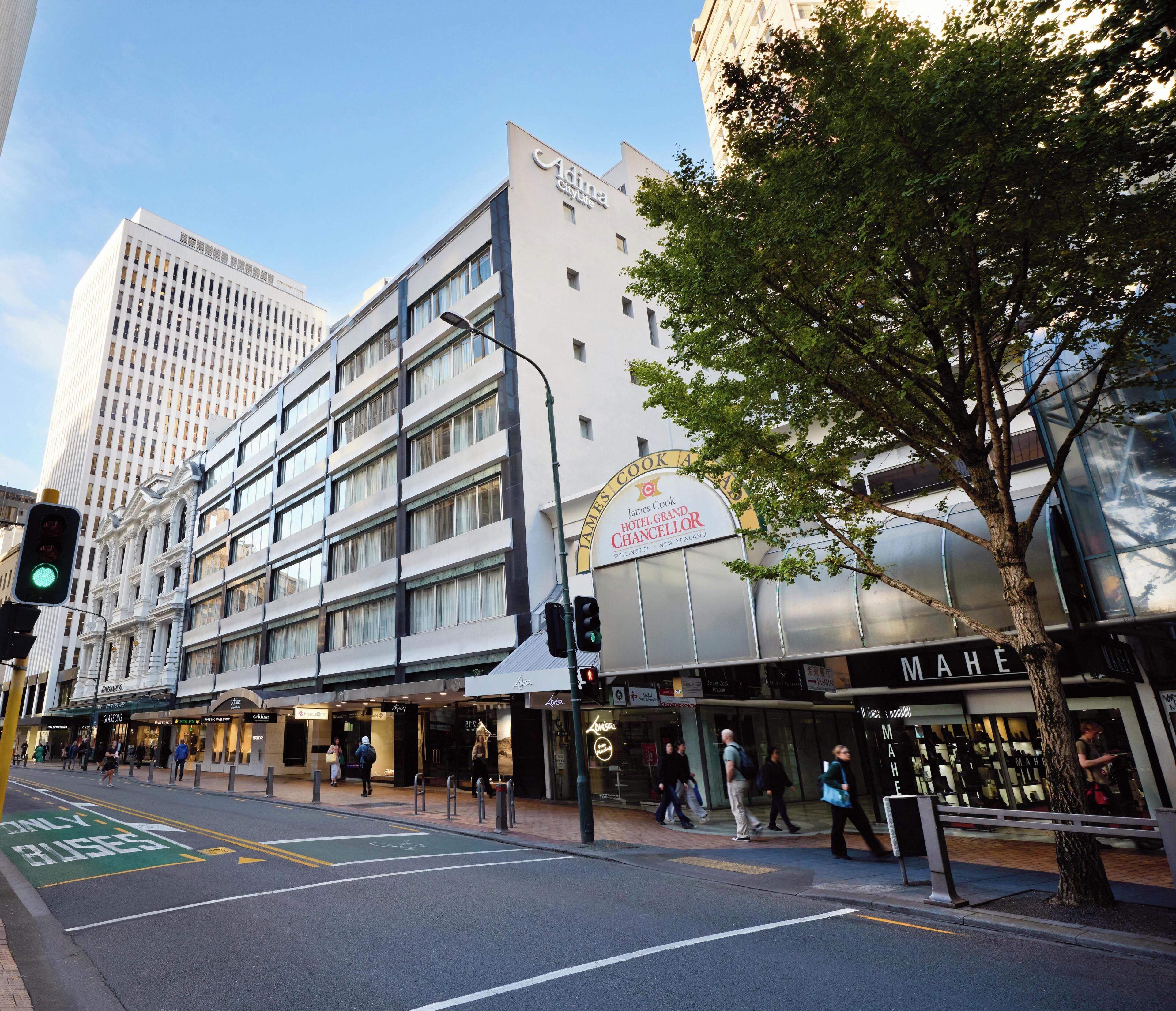 A hotel with a prominent sign for James Cook Hotel Grand Chancellor, a modern building with multiple floors, and a tree-lined street.