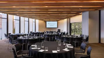 A conference room with round tables, black chairs, and a large screen displaying the hotel name.