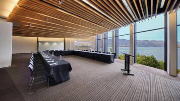 Un salón de conferencias con una larga mesa, sillas, un atril y grandes ventanales con vistas a la montaña.
