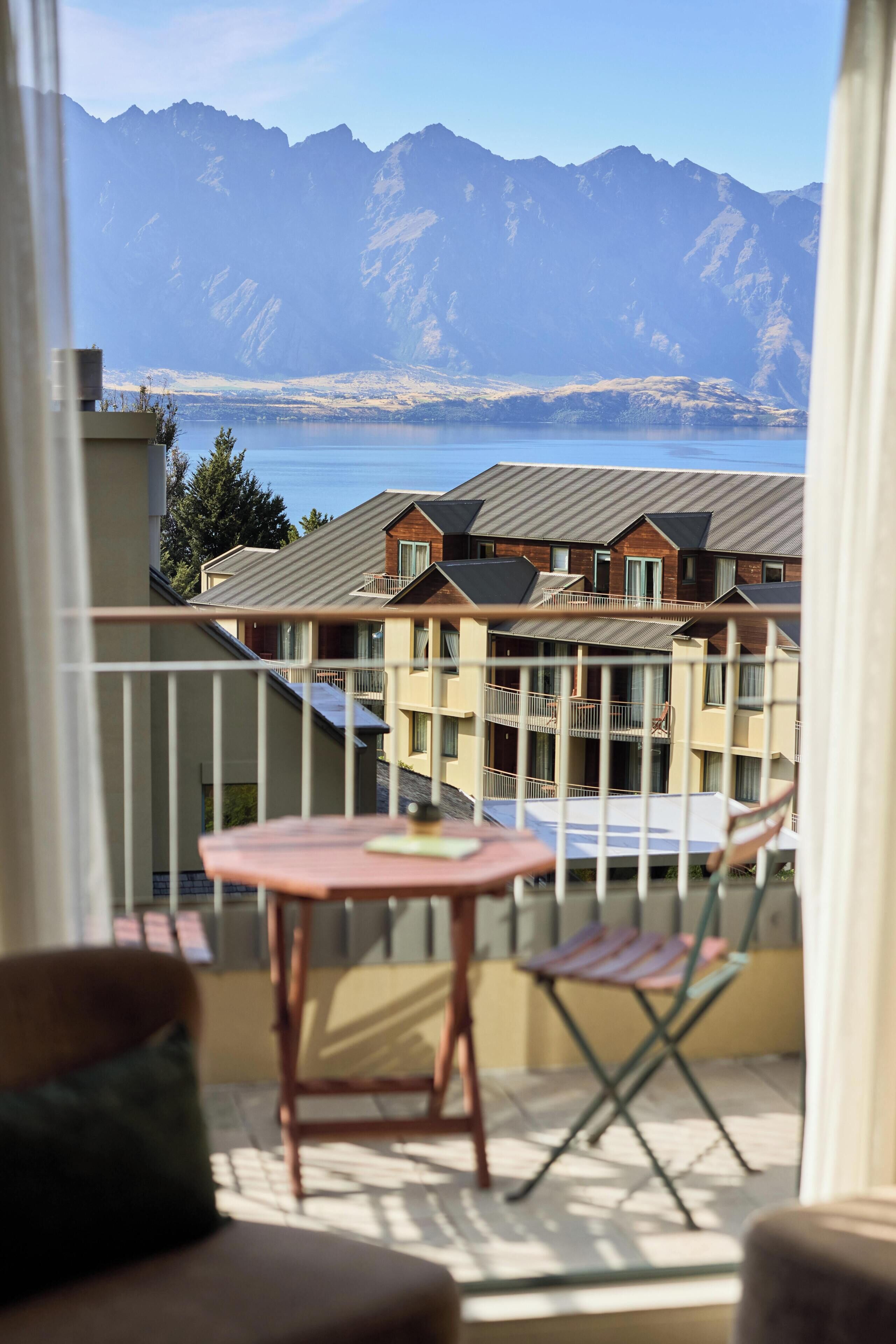 Un balcon avec une table et des chaises, donnant sur une montagne et un plan d’eau.