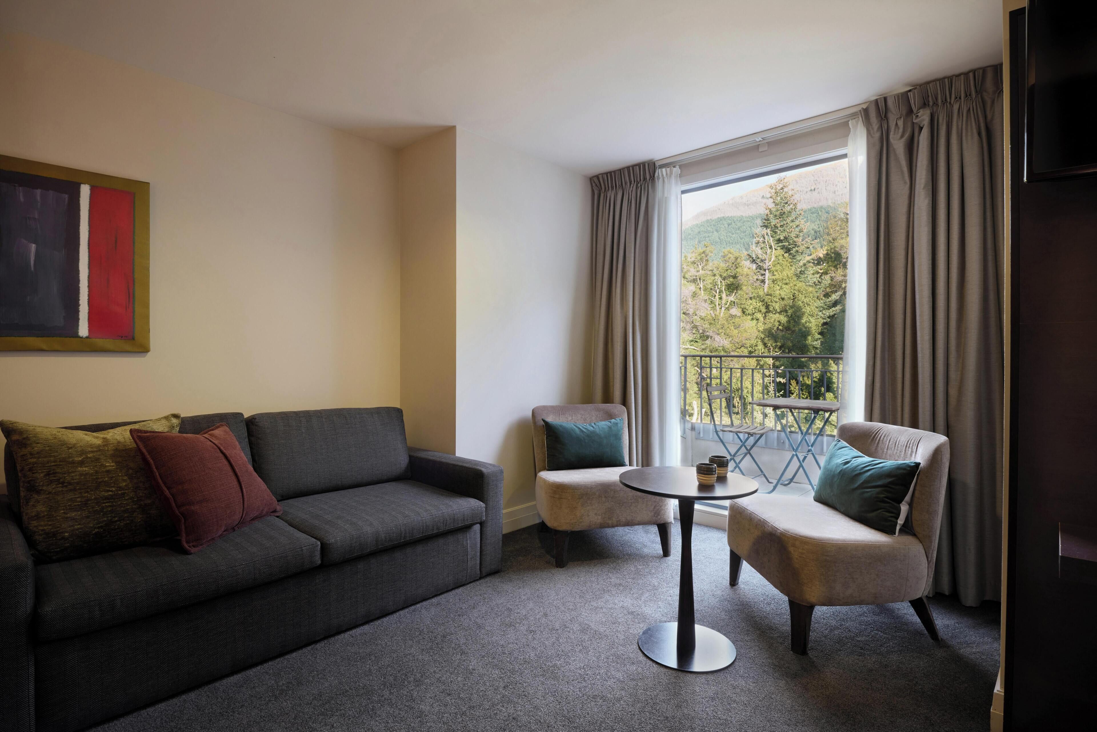 Habitación con sofá, dos sillones, una mesita redonda y vistas a un balcón con barandilla.