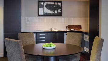 A modern kitchen with a dining table, chairs, and a bowl of green apples.