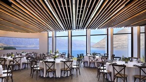A dining area with round tables, chairs, and a view of the sea through large windows. - Rendezvous Heritage Hotel Queenstown (Queenstown)