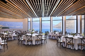 A dining area with round tables, chairs, and a view of the sea through large windows. - Rendezvous Heritage Hotel Queenstown (Queenstown)