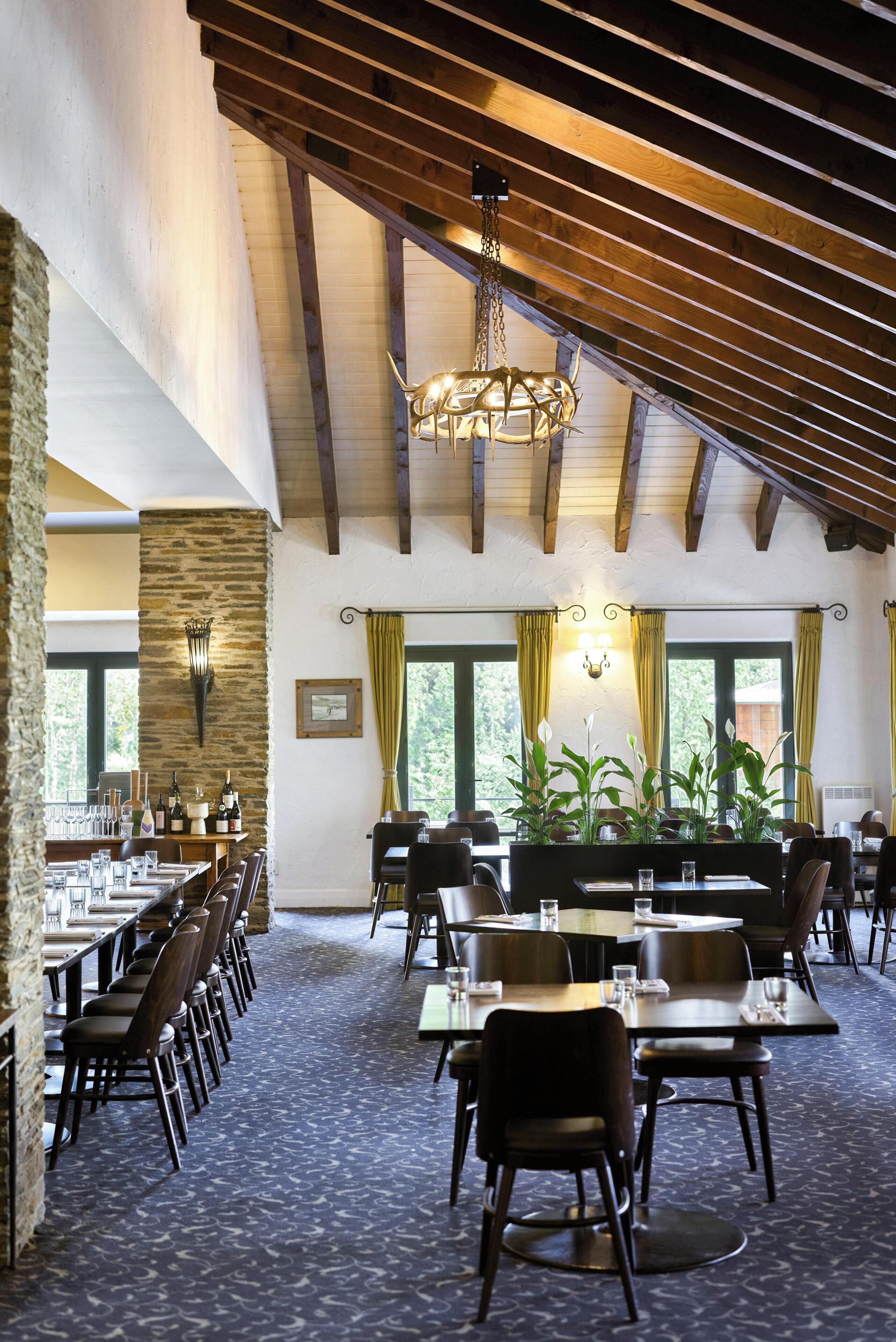 A dining area with tables and chairs, a chandelier, and a stone pillar.