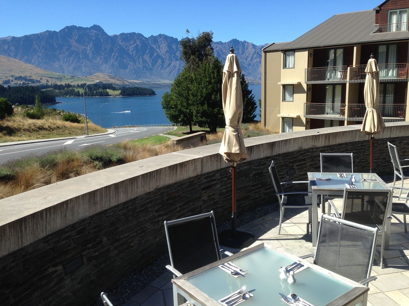 Um terraço com mesas e cadeiras, com vista para um lago e montanhas.