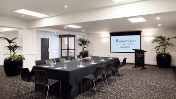 A conference room with a long table, chairs, a projector screen, and potted plants.