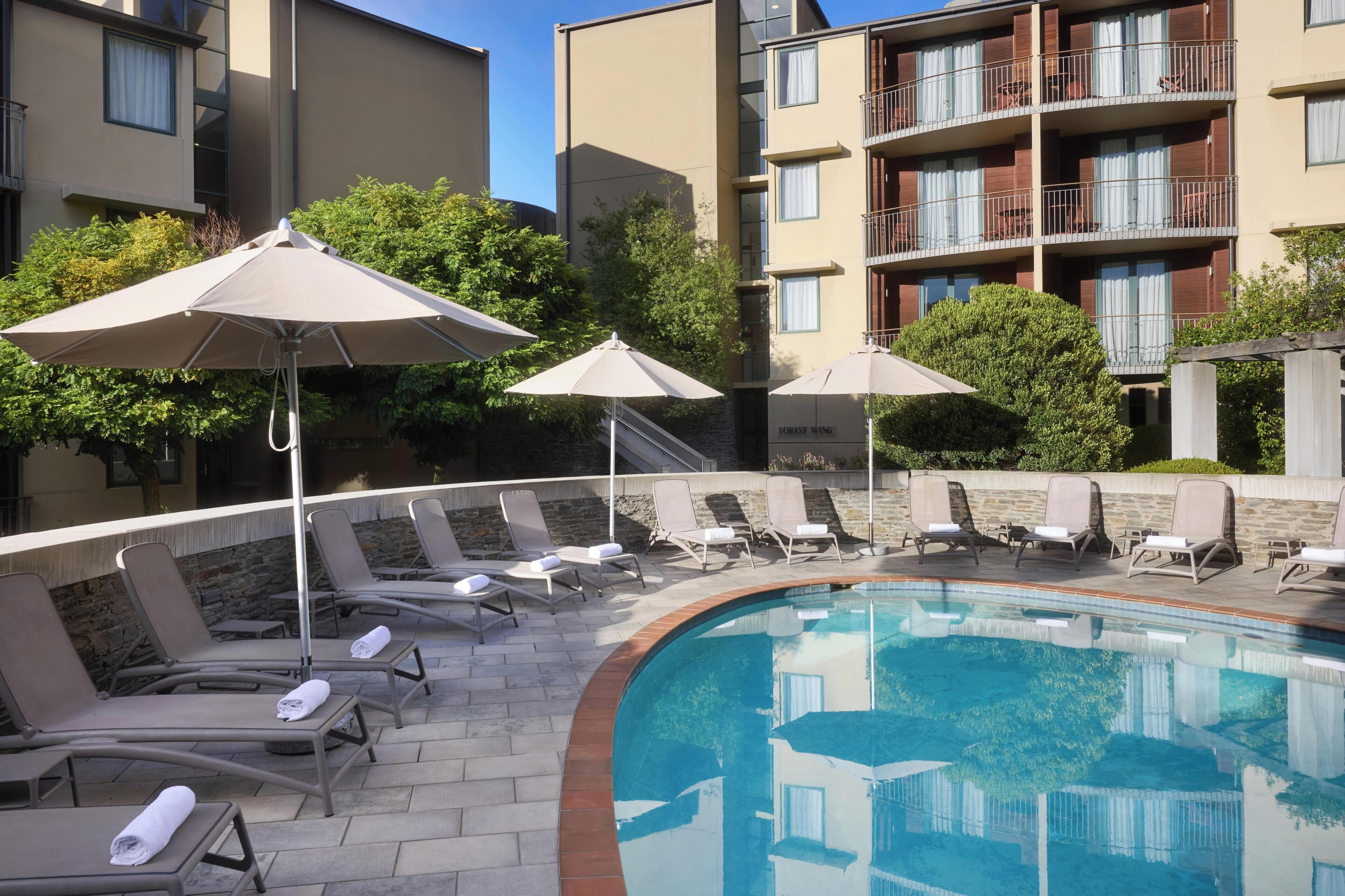 Piscina com espreguiçadeiras e guarda-sóis, cercada por edifícios de apartamentos.