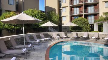Piscina com espreguiçadeiras e guarda-sóis, cercada por edifícios de apartamentos.