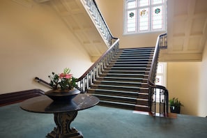Een statige trap met een leuning, een potplant en een tafel in een ruime binnenruimte.