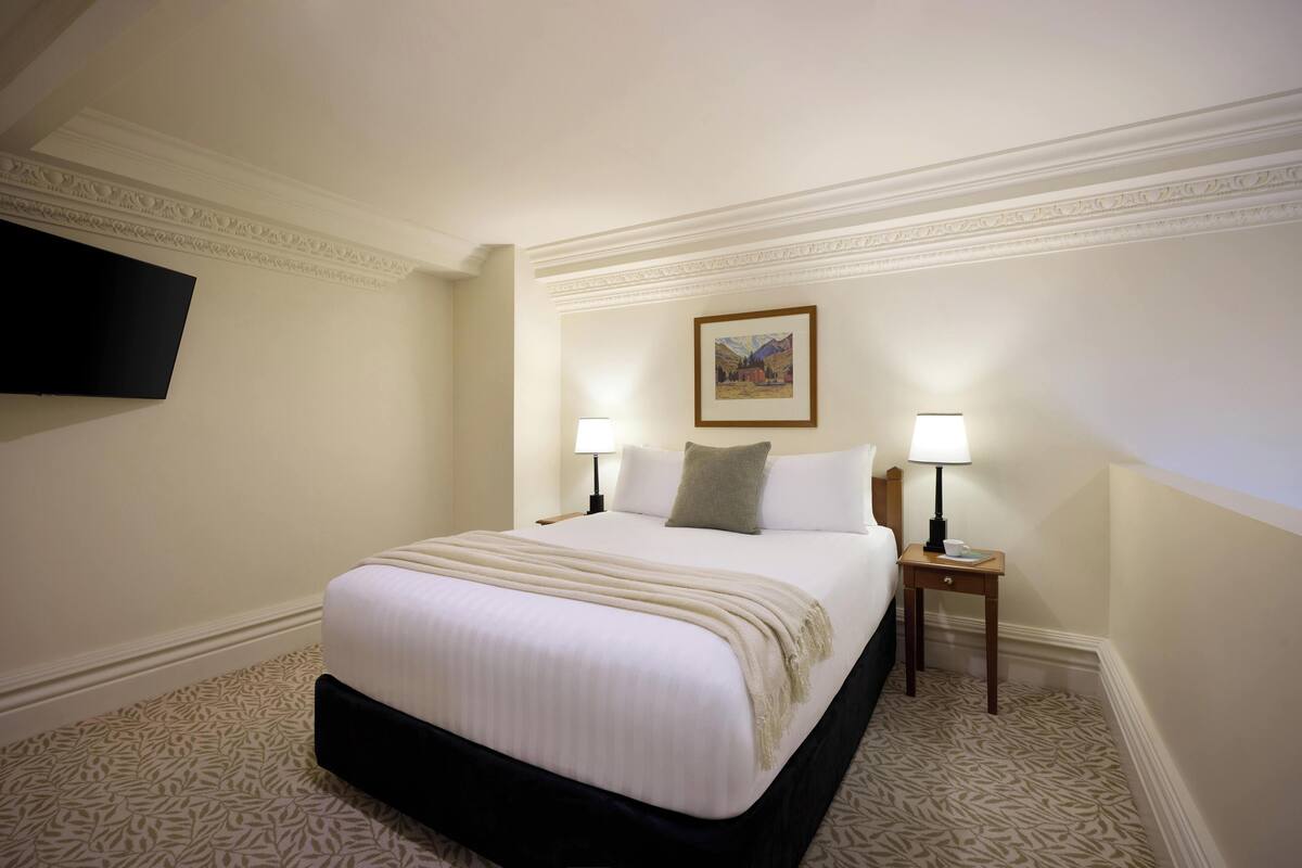 Een hotelkamer met een groot bed, twee nachtkastjes met lampen, een flatscreen televisie aan de muur en een ingelijst schilderij boven het bed.