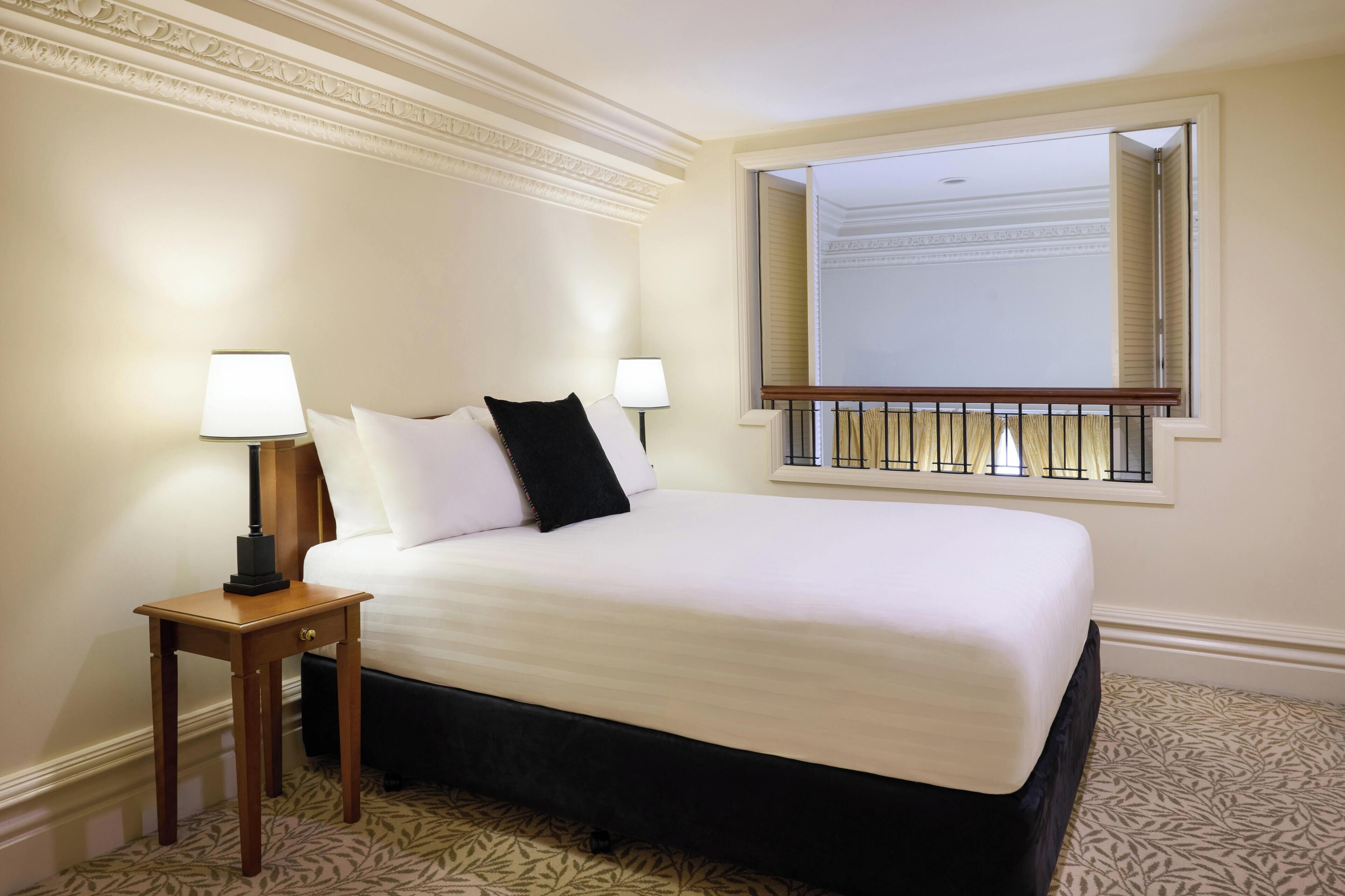 A hotel room with a large bed, two bedside lamps, a window with a view, and a patterned carpet.