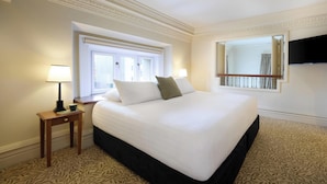 Hotelkamer met een groot bed, nachtkastje met lamp, raam en televisie aan de muur.