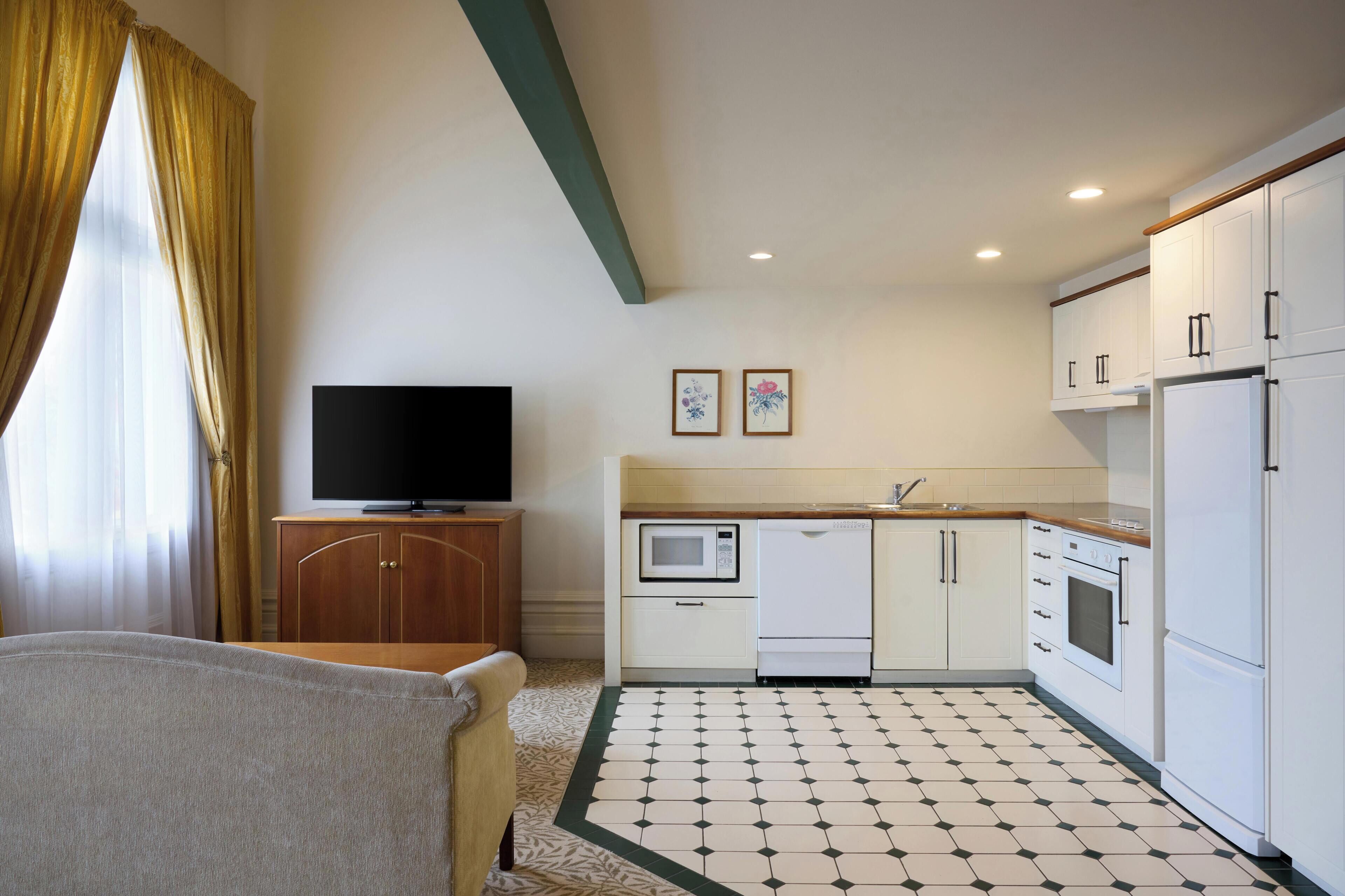 A compact kitchen with a microwave, oven, and refrigerator, a television on a wooden cabinet, and a patterned floor.