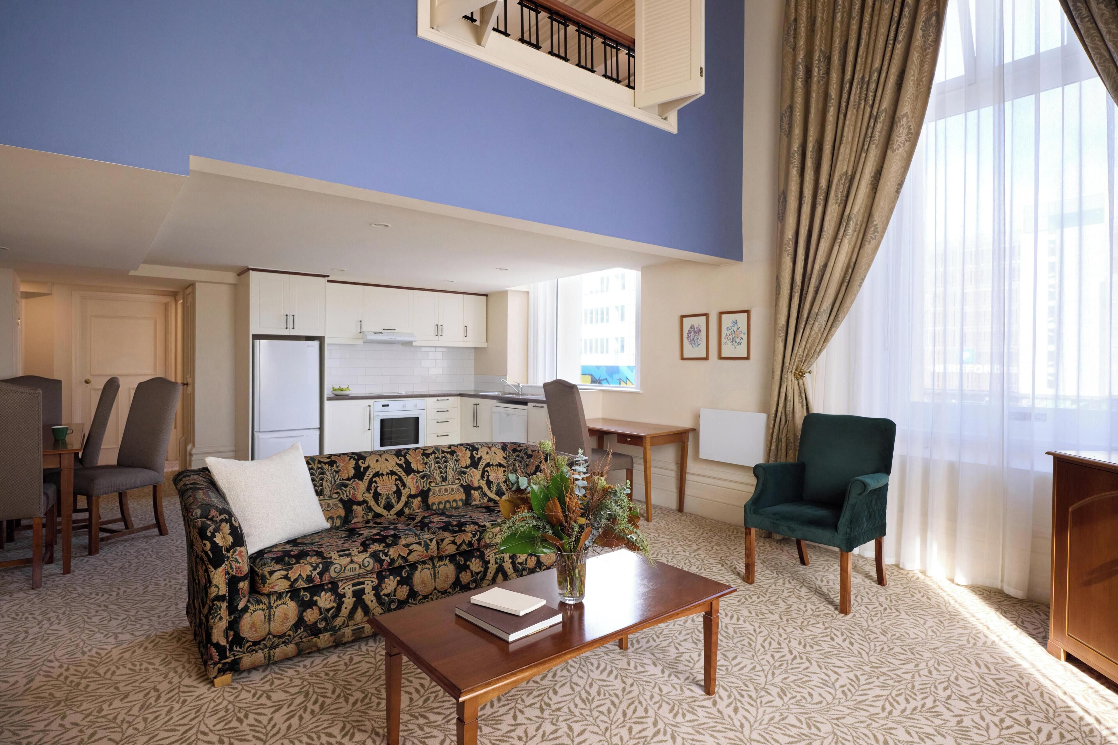 A living room with a sofa, a coffee table, a chair, a dining table, and a kitchen in the background.