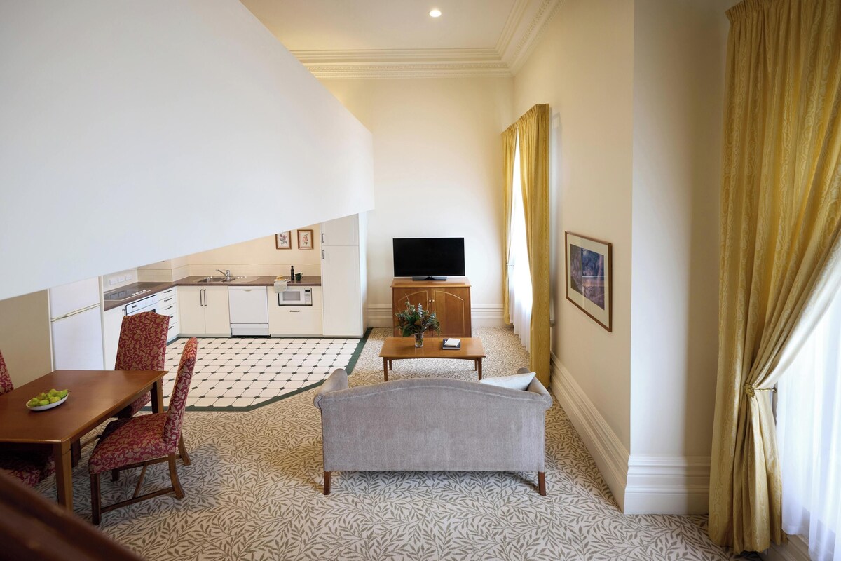 Ein Hotelzimmer mit Essbereich, einer Sitzecke, einem Fernseher und einer Küche im Hintergrund.
