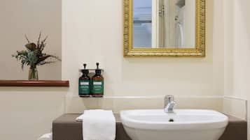 A bathroom with a white sink, a gold-framed mirror, and a vase with dried flowers on the wall.