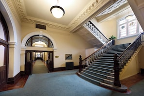 A grand staircase with a handrail, a carpeted floor, and a large arched doorway leading to another room.