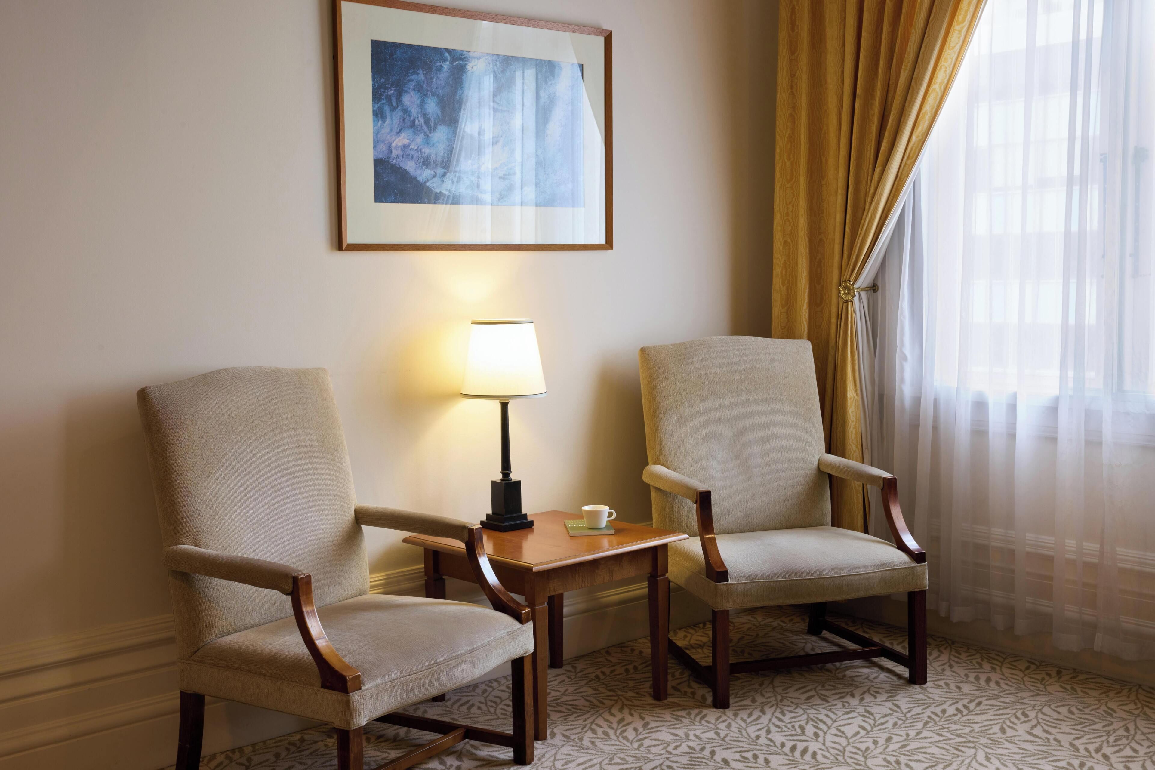 Due poltrone, un tavolino con una lampada, un quadro appeso al muro e una finestra con tende.