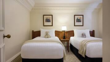 Een hotelkamer met twee bedden, een deur, een nachtkastje met een lamp en twee ingelijste foto's aan de muur.