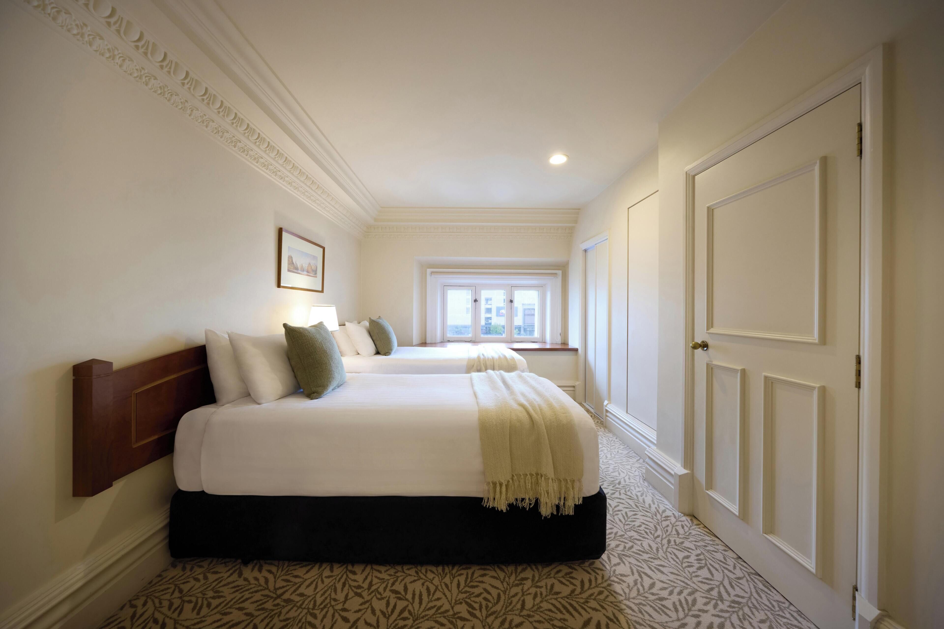 A hotel room with a large bed, a window, and a door.