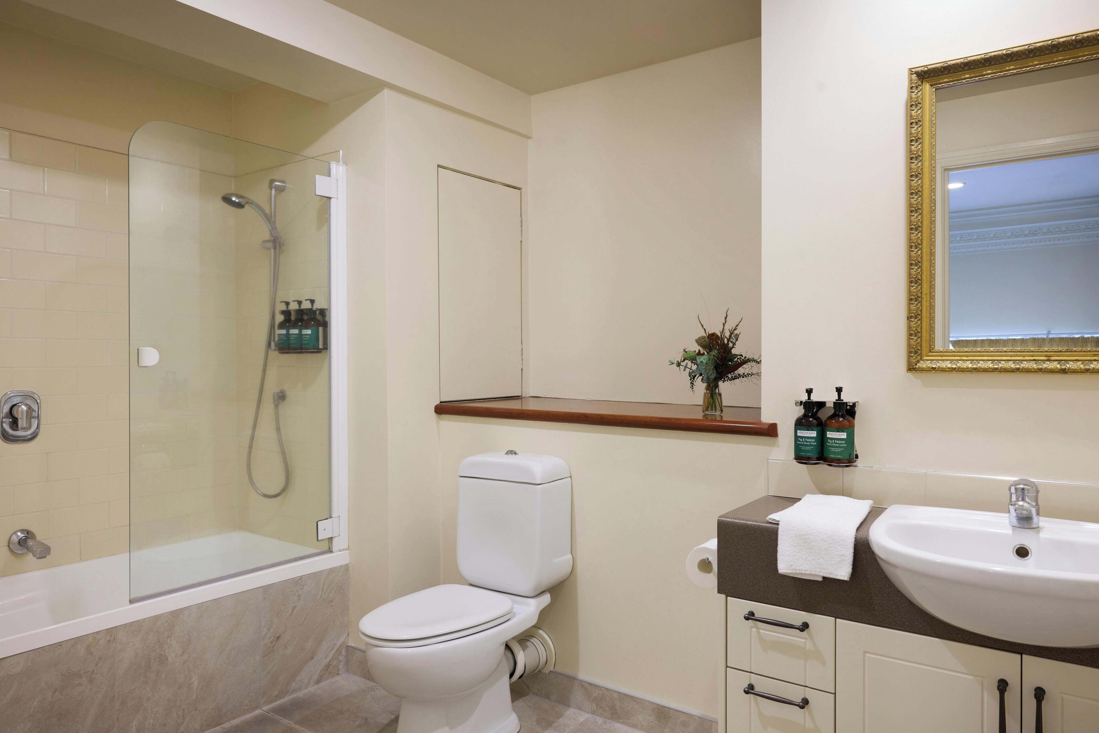 A bathroom with a glass-enclosed shower, a white toilet, a sink with a mirror, and toiletries on the countertop.