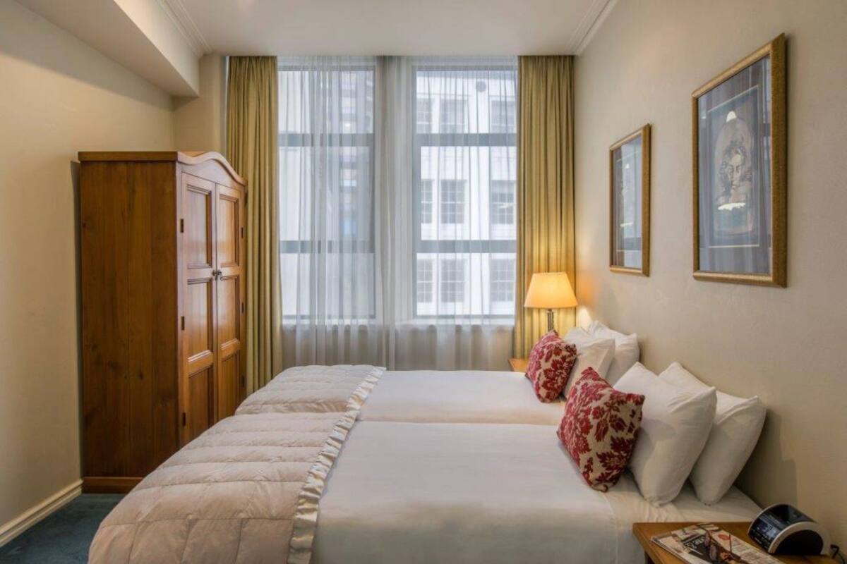 Une chambre d’hôtel avec deux lits, une armoire, une fenêtre avec des rideaux et une lampe.