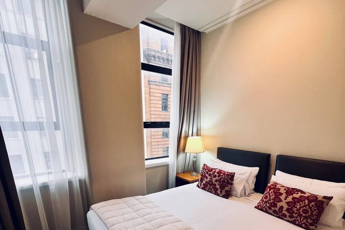 Une chambre d’hôtel avec un grand lit, une table de chevet, une lampe et une fenêtre avec des rideaux.