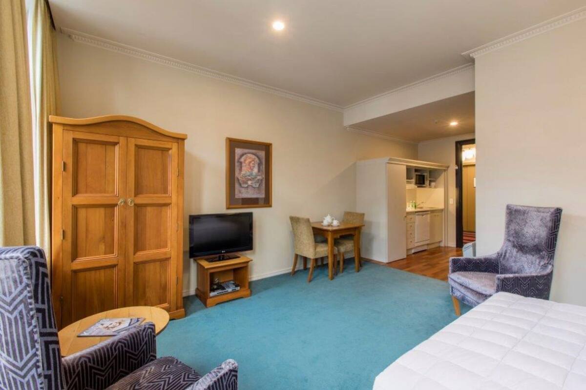 Une chambre d’hôtel équipée d’une grande armoire, d’un téléviseur, d’une table à manger et d’une chaise.