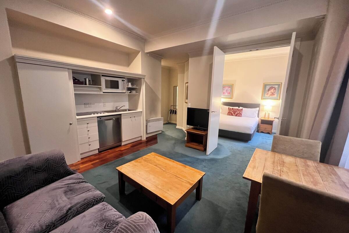 Une chambre d’hôtel compacte comprenant un coin cuisine, un canapé, une table basse, une télévision et un lit.