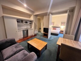 A compact hotel room with a kitchenette, a sofa, a coffee table, a TV, and a bed.