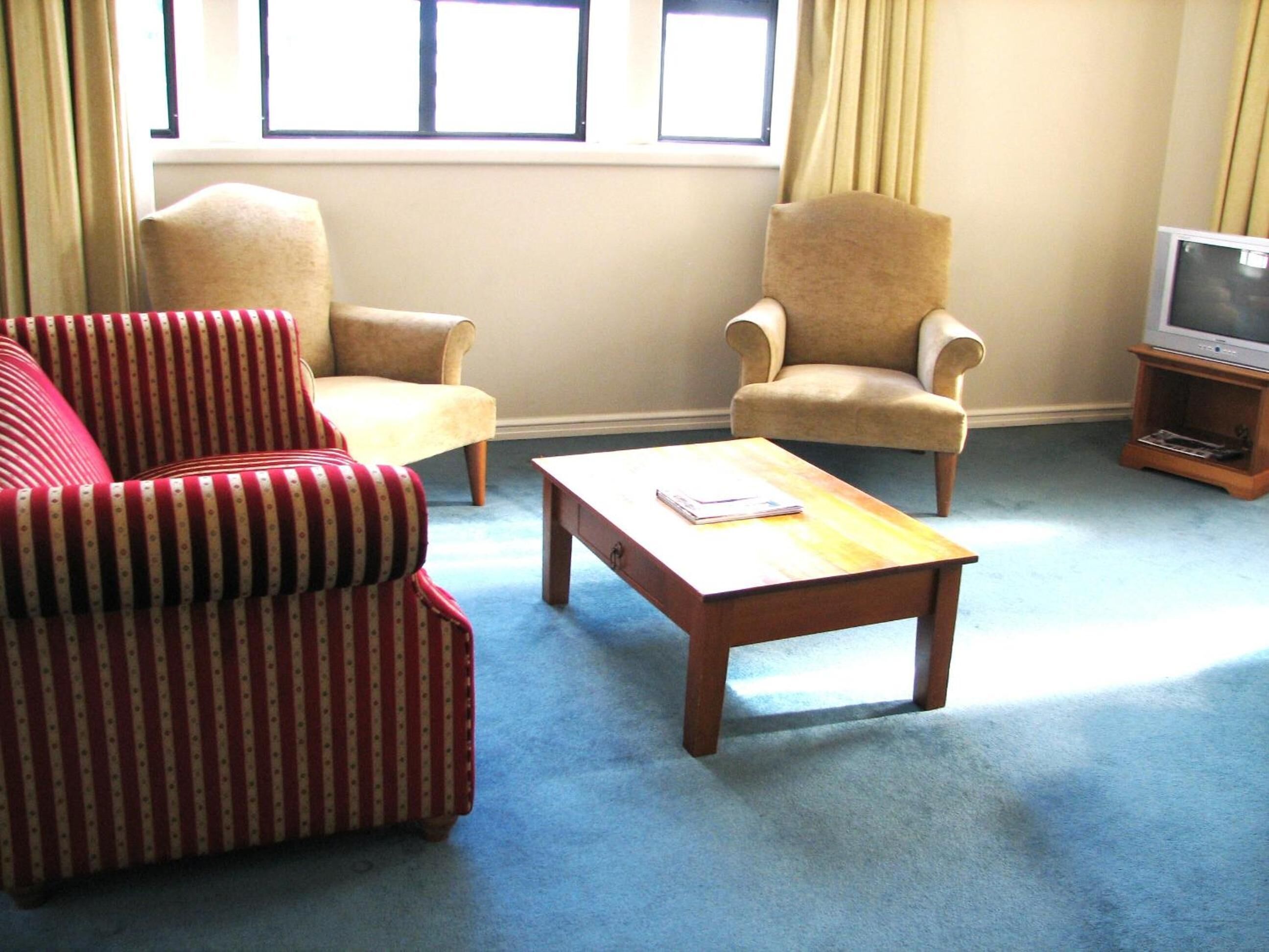 A living room with striped red and white sofa, two beige armchairs, a wooden coffee table, and a television on a wooden stand.