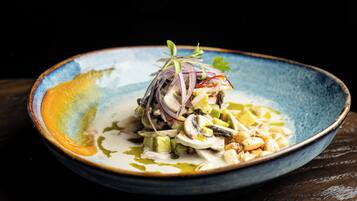 A blue ceramic plate with a seafood dish, garnished with red onion and herbs, on a dark wooden table.