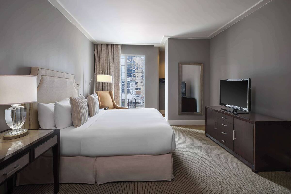 Een hotelkamer met een groot bed, een televisie, een bureau met een lamp en uitzicht op de stad.
