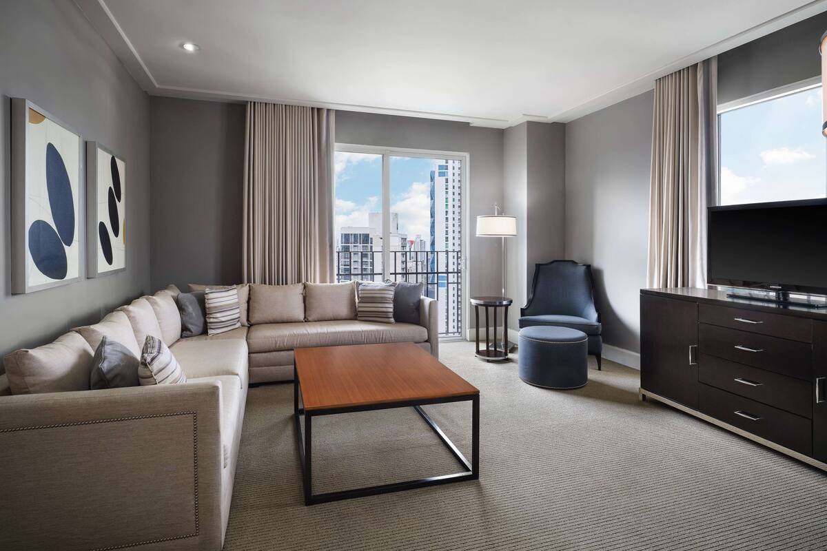 Een moderne hotelkamer met een bank, salontafel, televisie en uitzicht op de stad.