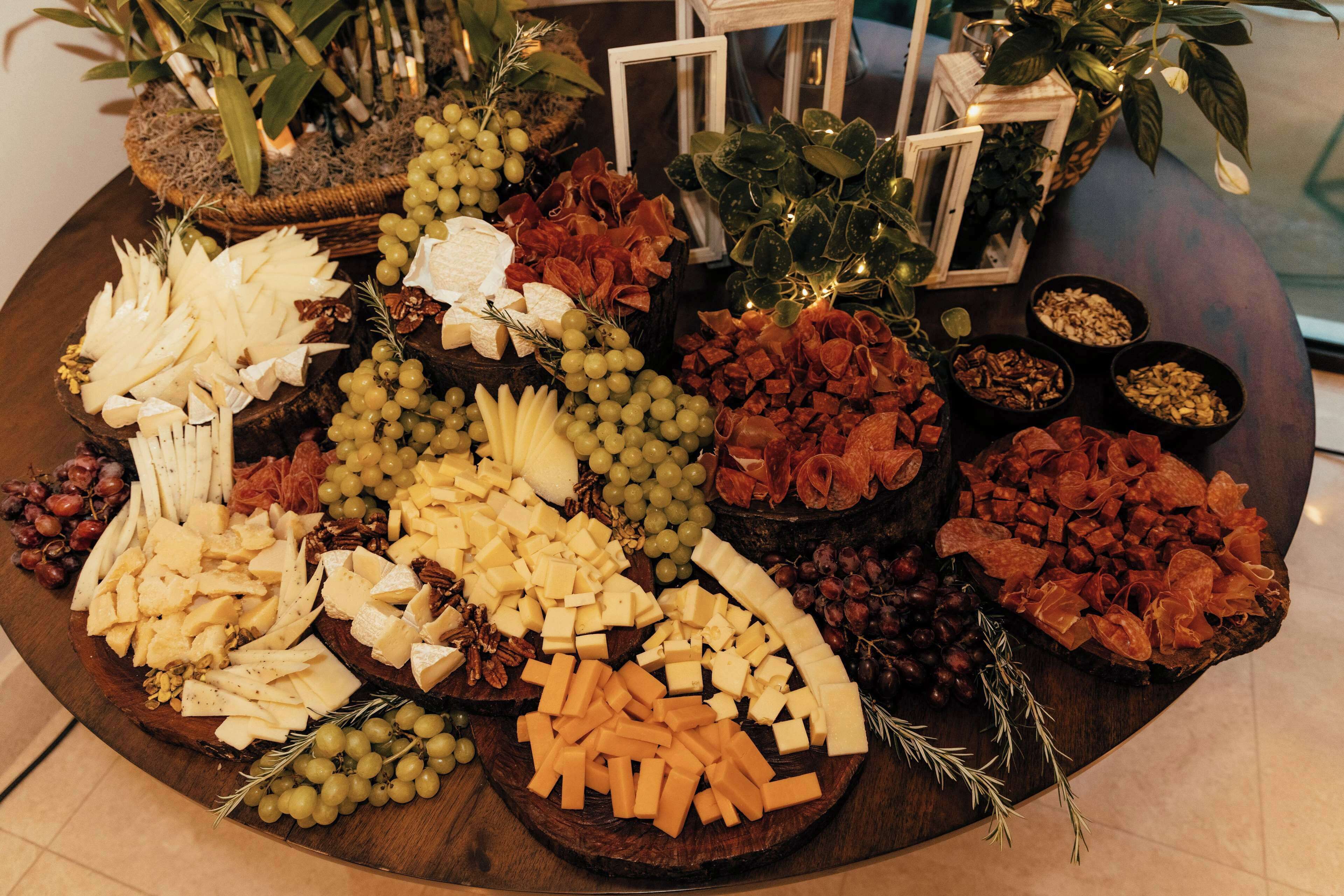 A cheese and fruit platter with various cheeses, grapes, and dried fruits on a wooden table.