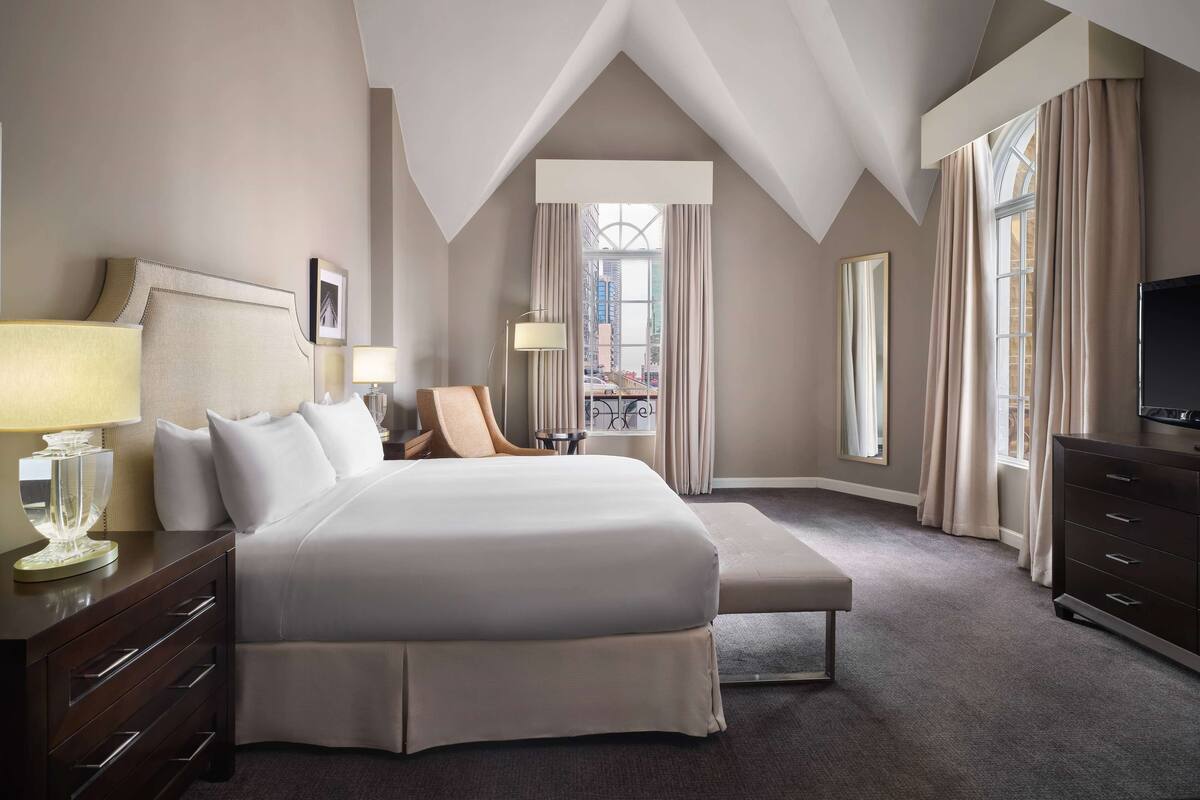 Hotelkamer met een groot bed, een bankje, een dressoir, een televisie en uitzicht op de stad.