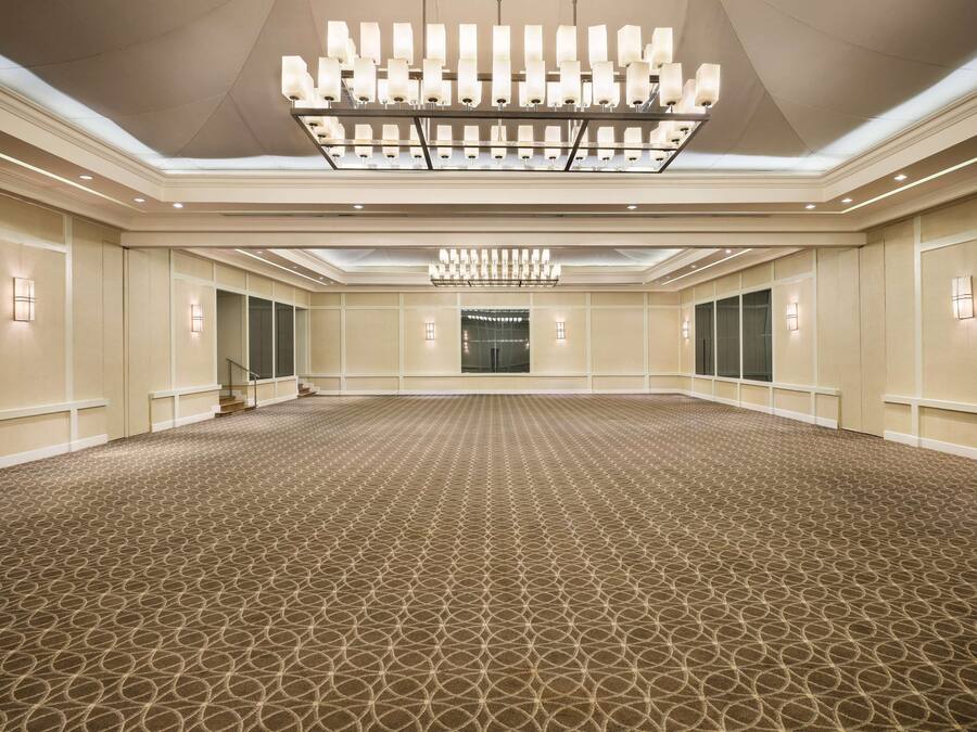 Una espaciosa y bien iluminada sala de conferencias con alfombra estampada, lámparas simétricas y una gran araña.