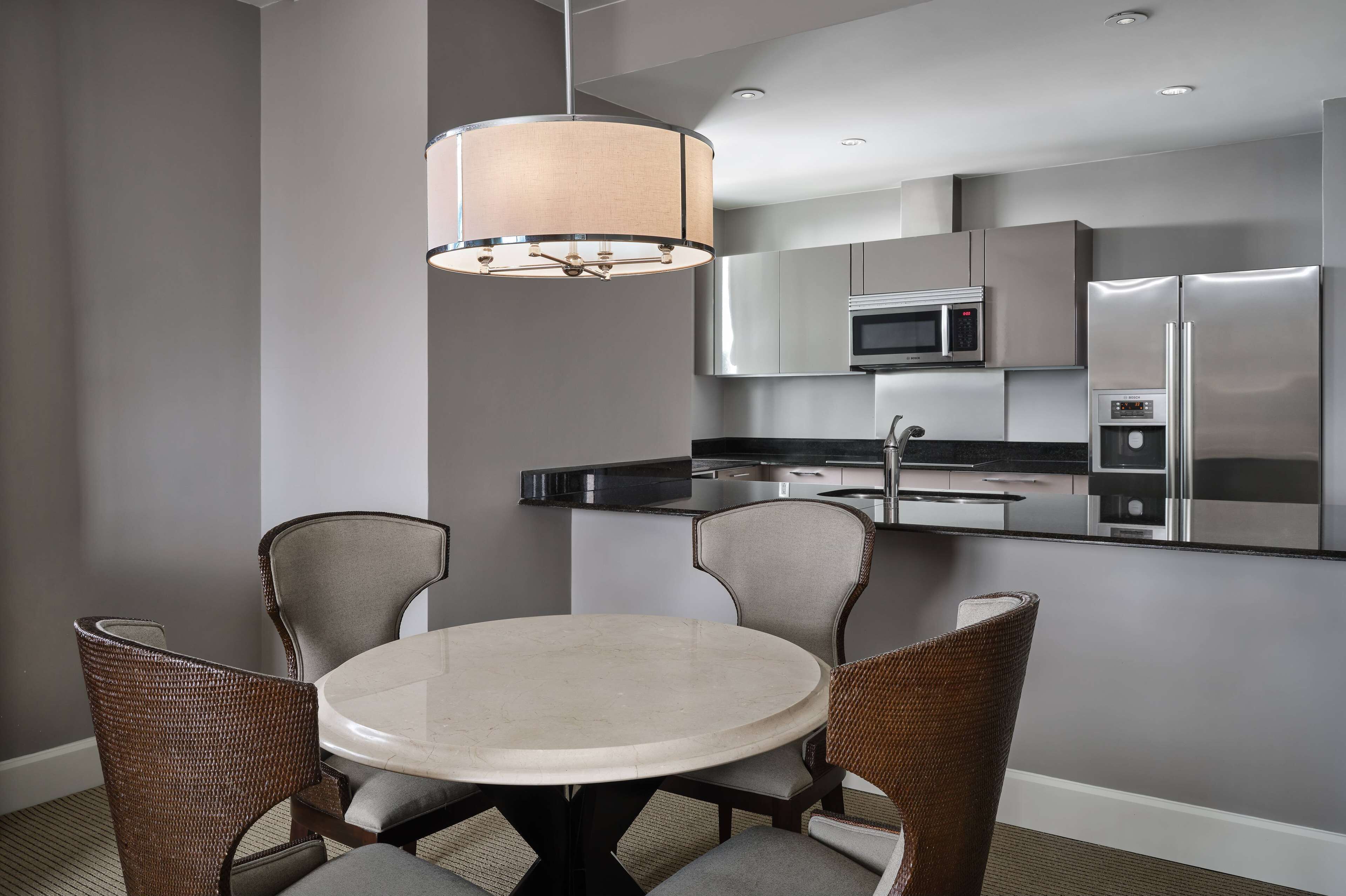 Una cocina moderna con electrodomésticos de acero inoxidable, una mesa redonda con cuatro sillas y una lámpara colgante.