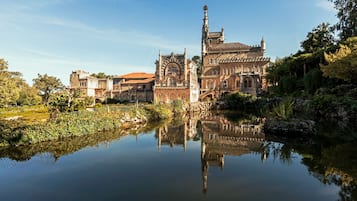 Un edificio histórico con una gran torre, reflejada en un cuerpo de agua tranquilo rodeado de vegetación.